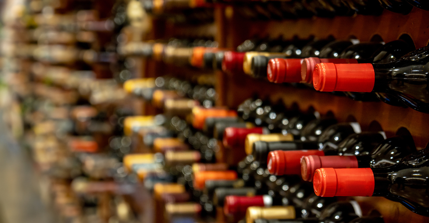 Bottles of black red wine lined up and stacked on wooden wine rack shelves from a private collection of a wine cellar in Spain.